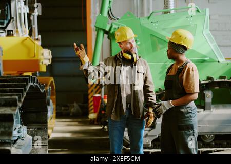 Medium long shot of two ethnically diverse male and female engineers working in heavy machinery production industry having conversation Stock Photo