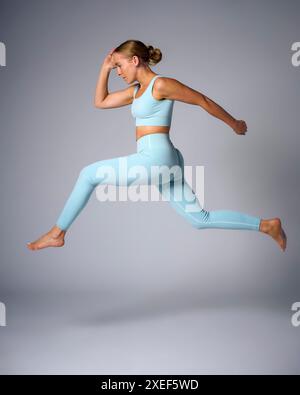 Studio Shot Of Woman Wearing Gym Fitness Clothing In Mid-Air Exercising On Grey Background Stock Photo