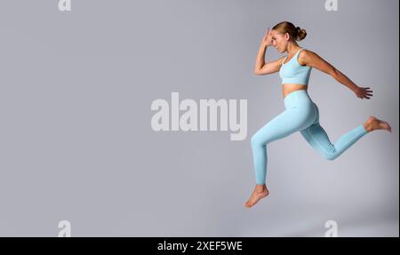 Studio Shot Of Woman Wearing Gym Fitness Clothing In Mid-Air Exercising On Grey Background Stock Photo