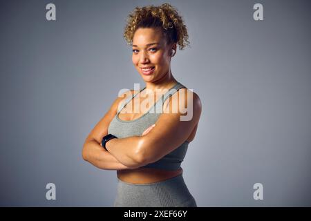 Studio Portrait Of Woman In Gym Fitness Clothing Streaming To Wireless Ear Buds From Fitness Tracker Stock Photo