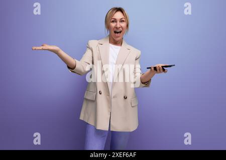 Blonde young woman in a jacket makes a payment using a phone on a studio background Stock Photo