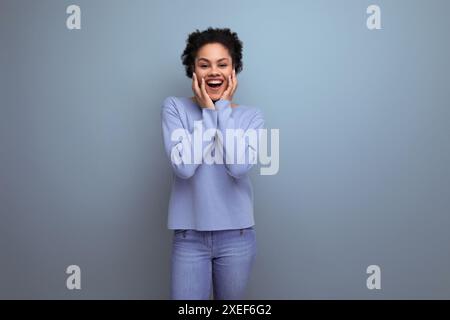 Positive energetic young brunette latin lady with afro curls in stylish spring clothes on isolated background Stock Photo