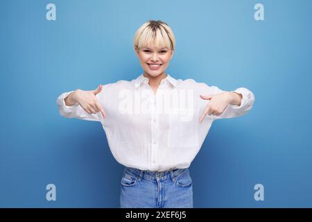 Young blond female student woman in white shirt pointing finger at promotional offer over isolated background Stock Photo