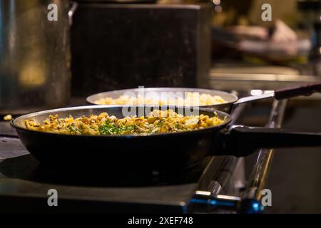Two pans of finished Kasnockerln (cheese dumplings) stand on the wood-fired stove in the Vorkaser of the Filzmoosalm near Großarl, Salzburg, Austria. Fried onions and freshly chopped chives cover the golden-brown cheese spaetzle mixture. Stock Photo