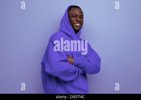 Cheerful cute ethnic 25 year old african man in a stylish hoodie with a hood on a blue background Stock Photo