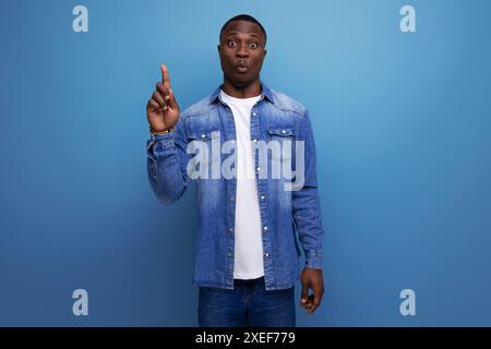 Surprised young attractive african man dressed in denim jacket and t-shirt on backgrounds with copy space Stock Photo