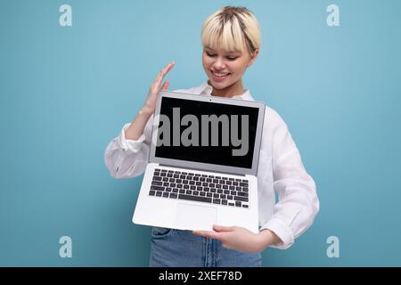 Young successful pretty blond office worker woman in a white shirt and jeans demonstrates a laptop screen with a mock-up for adv Stock Photo