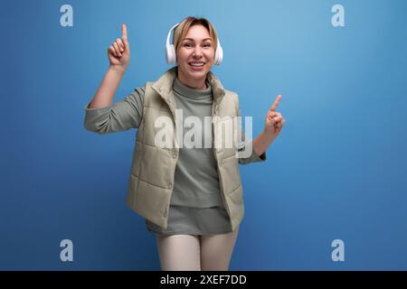Blond millennial woman listening to music in white headphones on studio background Stock Photo