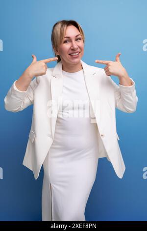 Young positive blond elegant female adult wearing jacket and dress smiling Stock Photo