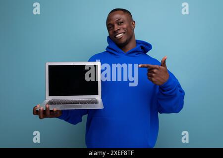 Handsome african young consultant in stylish hoodie with laptop to show ads on background with copy space Stock Photo