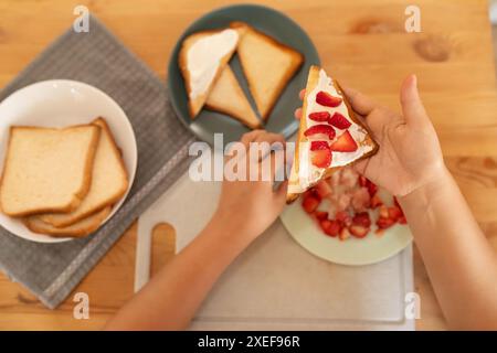 A woman makes breakfast, toast with sour cream and strawberries Stock Photo
