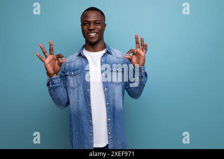 Young energetic positive with dark skin american guy dressed stylishly in jeans smiling against the background with copy space Stock Photo