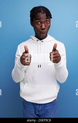 Positive young african guy in white sweatshirt showing like Stock Photo