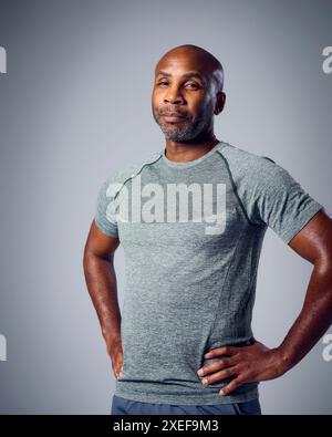Studio Portrait Of Serious Mature Man In Gym Fitness Clothing Folding Arms Against Grey Background Stock Photo