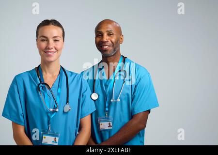 Studio Shot Of Smiling Male And Female Doctors In Scrubs Against White Background Stock Photo