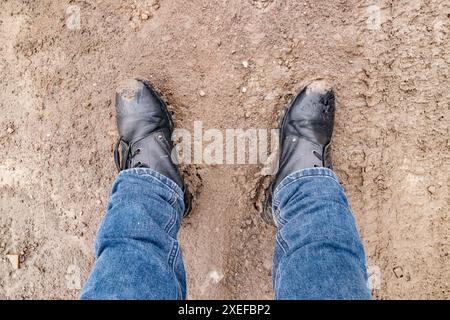 men's feet in jeans and boots standing in the mud, top view Stock Photo