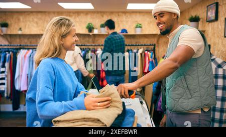 Woman Buying Clothes From Male Sales Assistant Using Barcode Scanner At Cash Desk In Fashion Store Stock Photo