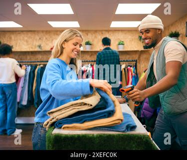 Woman Buying Clothes From Male Sales Assistant Using Barcode Scanner At Cash Desk In Fashion Store Stock Photo