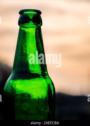 Against the evening sky the neck of an empty green beer bottle creates a minimalist scene, evoking the tranquility of twilight. Stock Photo