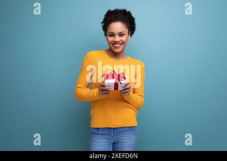 Young happy latin woman with afro hair holding gift box on studio background Stock Photo
