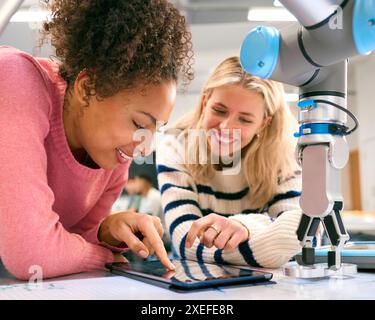 Two Female College Or University Engineering Students Using Digital Tablet To Control Robot Arm Stock Photo