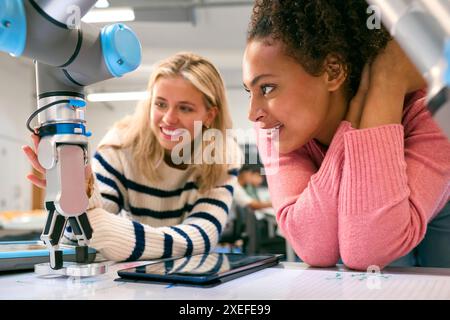 Two Female College Or University Engineering Students Using Digital Tablet To Control Robot Arm Stock Photo