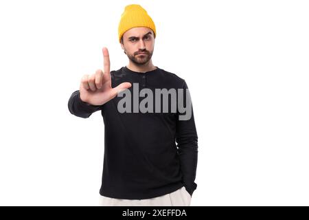 Young brunette confident male model with a beard dressed in a black jacket and a yellow hat Stock Photo