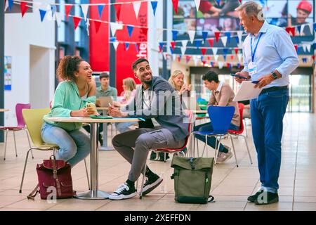 College Or University Students With Mobile Phone Working Together With Male Teacher In Study Area Stock Photo