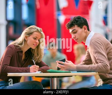 Two College Or University Students With Mobile Phone Working Together In Study Area Stock Photo