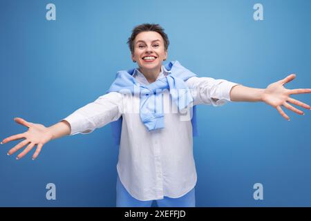 Kind young dark-haired woman with sticking hair in a white shirt stretches out her arms for a hug Stock Photo