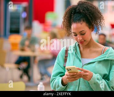 Smiling Female University Student Standing Inside College Building Using Mobile Phone Stock Photo