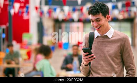 Smiling Male University Student Standing Inside College Building Using Mobile Phone Stock Photo