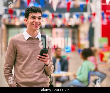 Smiling Male University Student Standing Inside College Building Using Mobile Phone Stock Photo