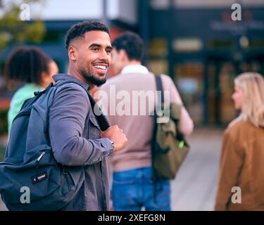 Portrait Of Male University Student Looking Over Shoulder With Friends Outside College Buildings Stock Photo