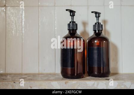 Close-up layouts with brown plastic bottles with dispensers in the bathroom. Mock-ups of shampoo or gel tubes with black empty l Stock Photo