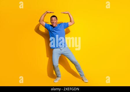 Full length photo of handsome young guy hold up ceiling empty space dressed stylish blue garment isolated on yellow color background Stock Photo