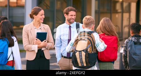 Male And Female Secondary Or High School Teachers Outside School Building Talking With Students Stock Photo