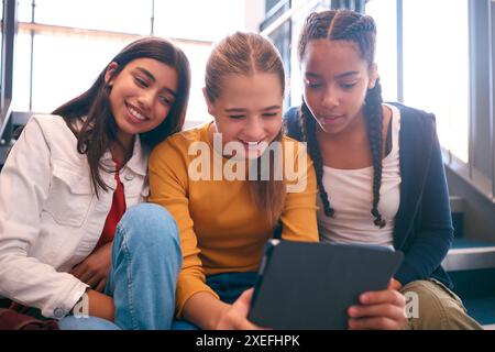 Three Female Secondary Or High School Pupils Inside School Building On Stairs With Digital Tablet Stock Photo