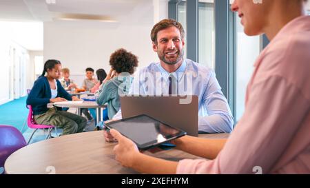 Secondary Or High School Teachers With Laptop And Digital Tablet In Study Area With Pupils Stock Photo