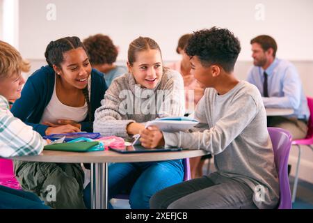 Secondary Or High School Students Collaborating In Study Area With Teachers In Background Stock Photo