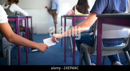 Close Up Of Two Male Secondary Or High School Pupils Passing Note During Lesson Stock Photo