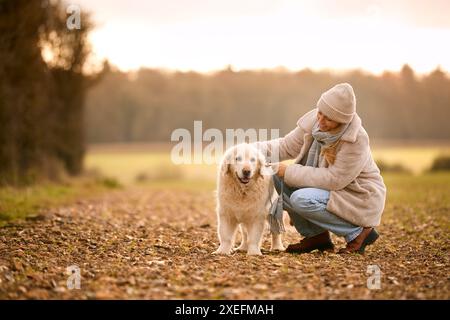 Woman Stroking Golden Retriever Dog On Walk Around Field In Autumn Countryside Stock Photo