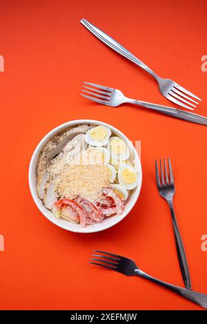 Top view of Caesar salad with lettuce, tomatoes, eggs, croutons, chicken and sauce in paper bowl Stock Photo