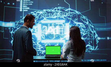 Startup coworkers brainstorming ways to use AI on chroma key notebook to improve data driven decisions. Technicians using mockup laptop to improve artificial intelligence tech, camera B Stock Photo