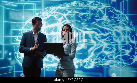 Coworkers solving tasks on laptop and tablet, running artificial intelligence programming scripts. IT staff members using devices to write lines of code for AI applications development, camera B Stock Photo