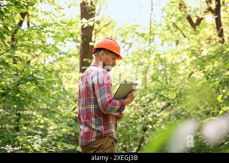 Forester with laptop examining plants in forest Stock Photo