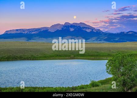 full moon setting over sawtooth ridge and a prairie pond near choteau, montana Stock Photo