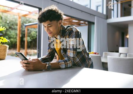 Smiling young man using smartphone while leaning on kitchen counter at home Stock Photo