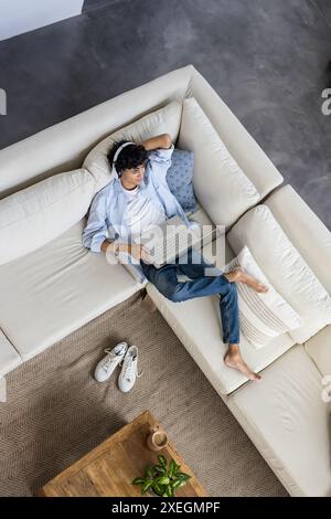 Relaxing on sofa, young man using laptop and wearing headphones at home Stock Photo