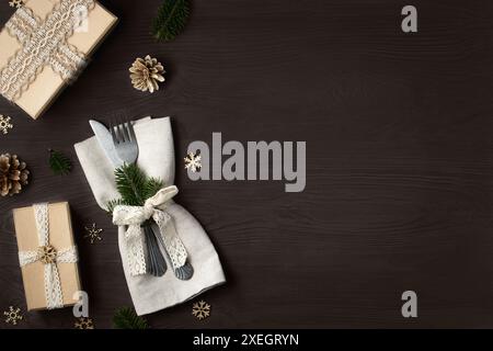 Christmas dinner concept. Forks with a knife on a napkin and Christmas decorations made from natural materials on a dark wooden table. Top view, flat Stock Photo